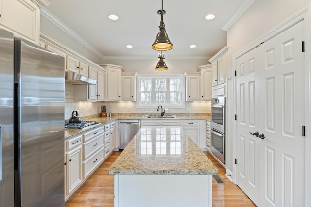 kitchen featuring a kitchen island, decorative light fixtures, sink, light stone counters, and stainless steel appliances