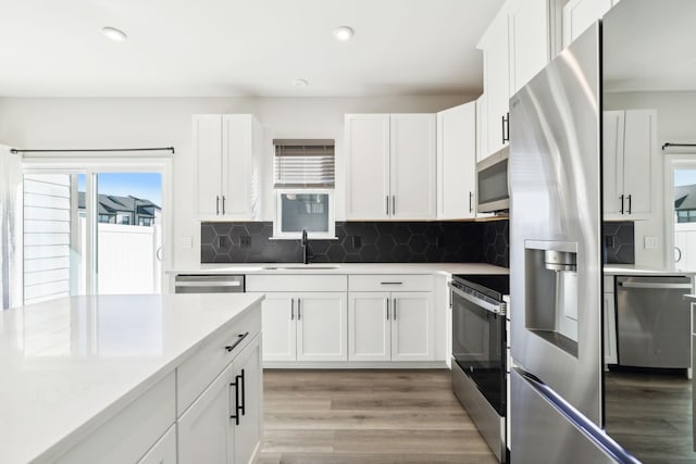 kitchen with sink, tasteful backsplash, light wood-type flooring, stainless steel appliances, and white cabinets