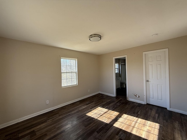 unfurnished bedroom featuring ensuite bathroom and dark hardwood / wood-style floors