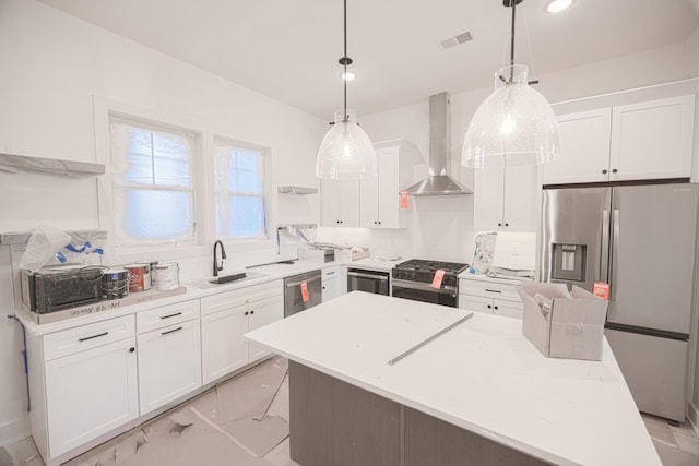 kitchen featuring wall chimney exhaust hood, stainless steel appliances, hanging light fixtures, and white cabinets