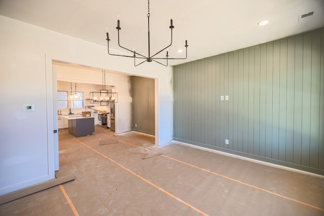 unfurnished dining area with sink, wooden walls, concrete flooring, and a chandelier