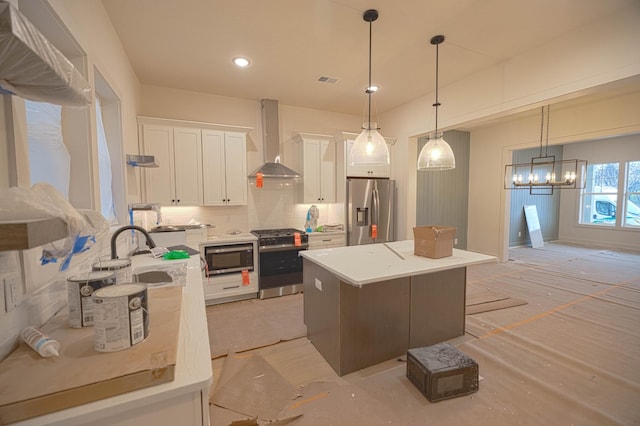 kitchen featuring decorative light fixtures, sink, white cabinets, stainless steel appliances, and wall chimney exhaust hood