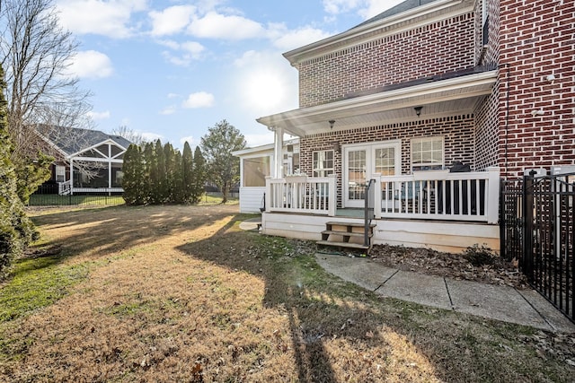 back of property featuring a trampoline, a wooden deck, a lawn, and a sunroom