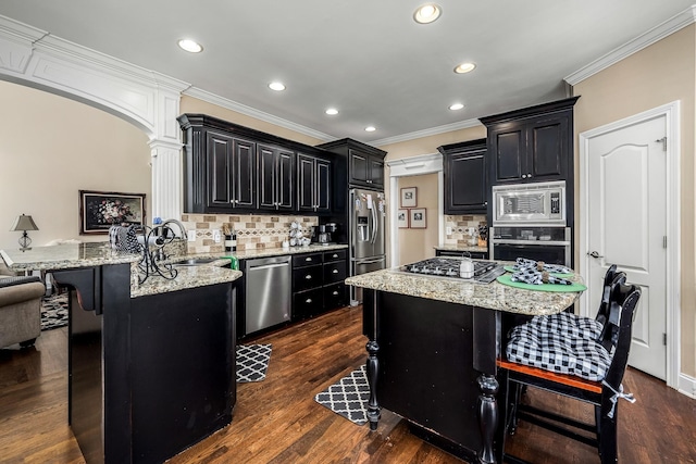 kitchen featuring a breakfast bar, sink, light stone counters, appliances with stainless steel finishes, and a kitchen island