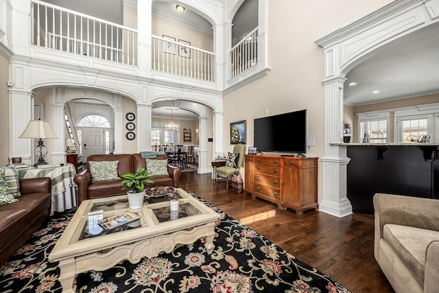 living room featuring decorative columns, crown molding, a notable chandelier, and dark hardwood / wood-style flooring