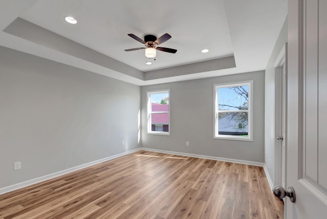 unfurnished room featuring ceiling fan, light hardwood / wood-style floors, and a tray ceiling