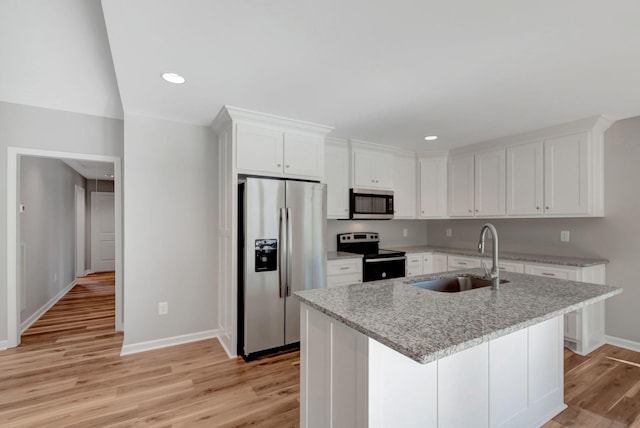 kitchen featuring sink, appliances with stainless steel finishes, light stone countertops, white cabinets, and a center island with sink