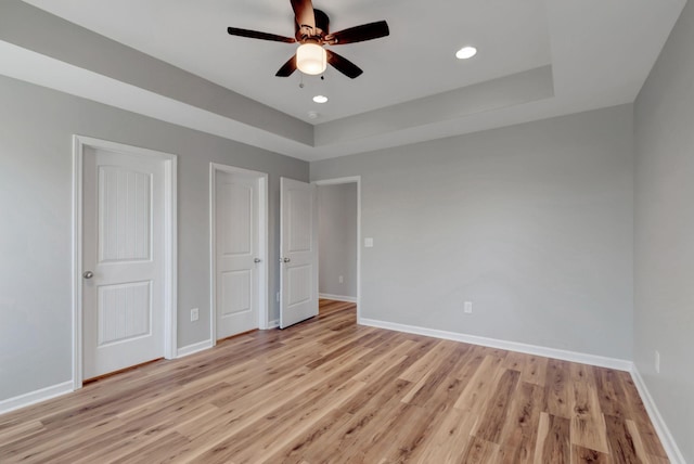 unfurnished bedroom with a tray ceiling, ceiling fan, and light wood-type flooring