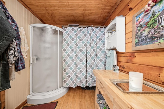 bathroom with a shower with shower door, wood walls, wood-type flooring, wooden ceiling, and vanity