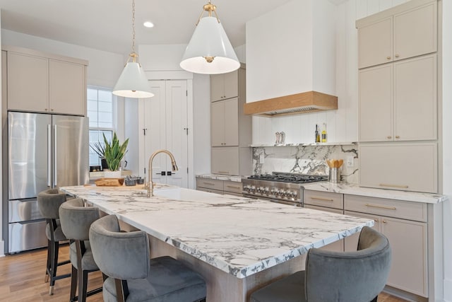 kitchen featuring stainless steel appliances, decorative light fixtures, custom range hood, and a center island with sink