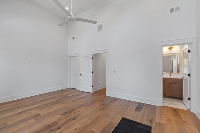 interior space featuring connected bathroom, a towering ceiling, ceiling fan, and light wood-type flooring