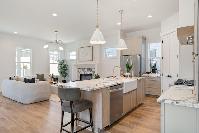 kitchen with appliances with stainless steel finishes, pendant lighting, an island with sink, light stone countertops, and light wood-type flooring