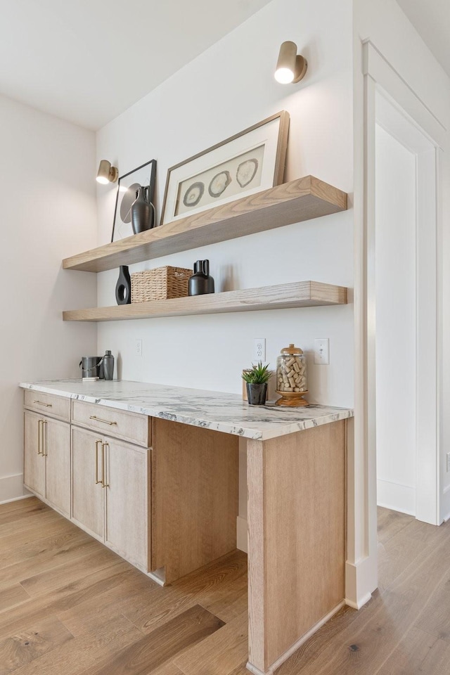 bar with light stone counters, light hardwood / wood-style floors, and light brown cabinets