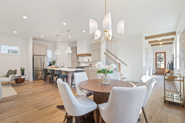 dining room featuring beam ceiling, sink, an inviting chandelier, and light hardwood / wood-style flooring