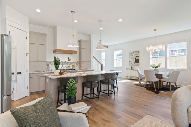 kitchen featuring hanging light fixtures, stainless steel fridge, light hardwood / wood-style floors, and an island with sink