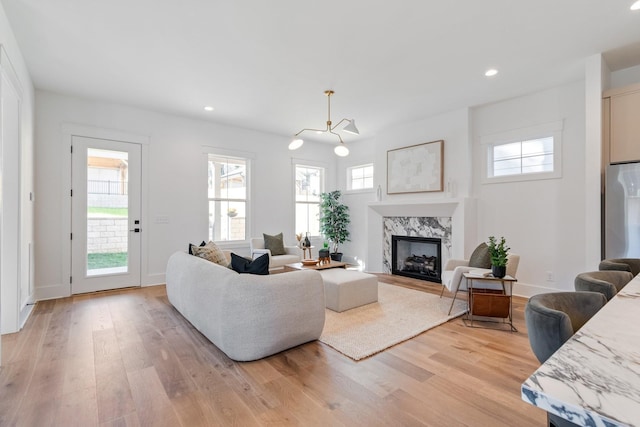 living room with a high end fireplace, light hardwood / wood-style floors, a chandelier, and a healthy amount of sunlight