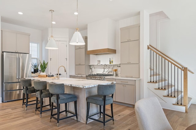 kitchen featuring premium range hood, high end refrigerator, hanging light fixtures, light hardwood / wood-style floors, and a center island with sink