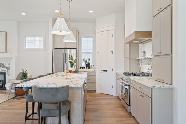 kitchen featuring premium range hood, pendant lighting, an island with sink, sink, and stainless steel appliances