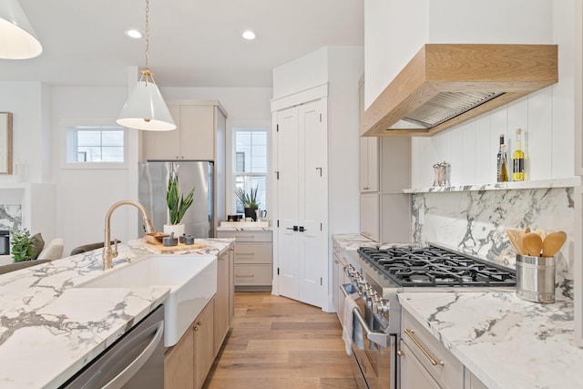 kitchen with pendant lighting, sink, stainless steel appliances, light stone countertops, and light wood-type flooring