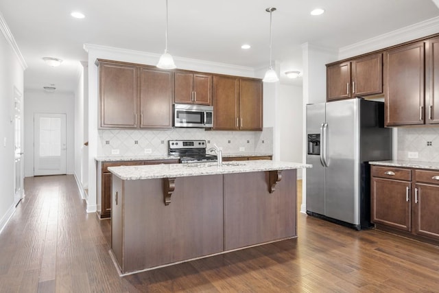 kitchen with a breakfast bar area, appliances with stainless steel finishes, an island with sink, pendant lighting, and light stone countertops