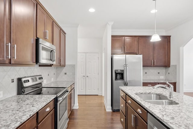 kitchen featuring appliances with stainless steel finishes, decorative light fixtures, sink, ornamental molding, and light stone countertops