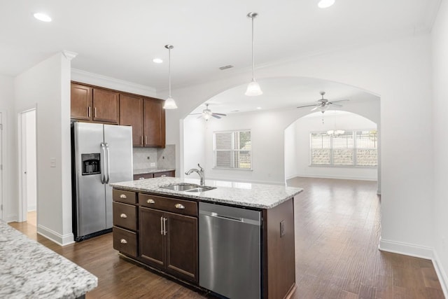 kitchen with sink, light stone counters, a center island with sink, appliances with stainless steel finishes, and pendant lighting