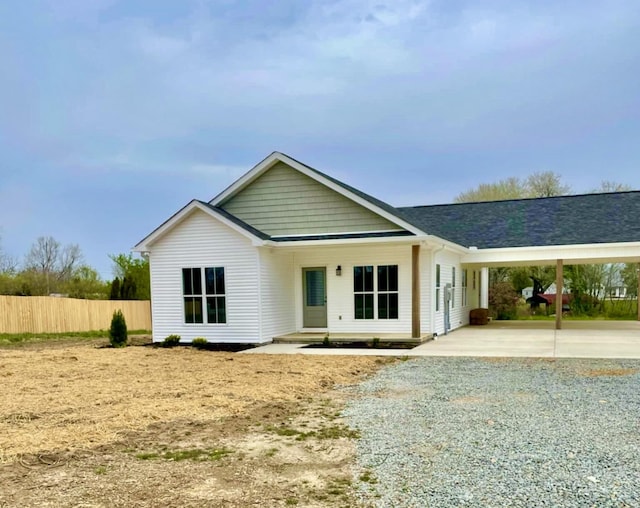 ranch-style house with gravel driveway, a carport, fence, and a shingled roof