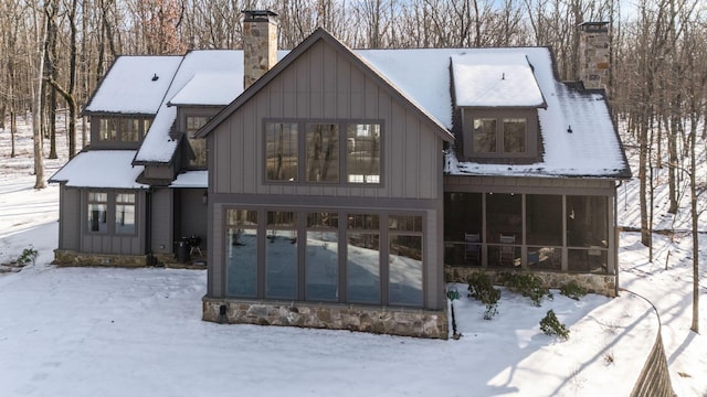 snow covered rear of property featuring a sunroom