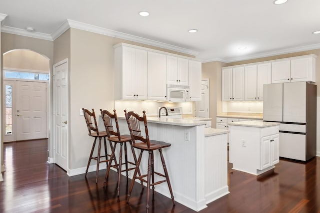 kitchen with dark wood-type flooring, white appliances, an island with sink, and white cabinets