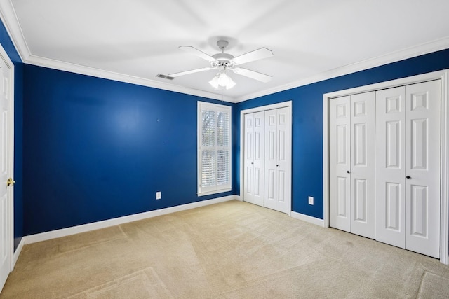 unfurnished bedroom with crown molding, light colored carpet, ceiling fan, and two closets