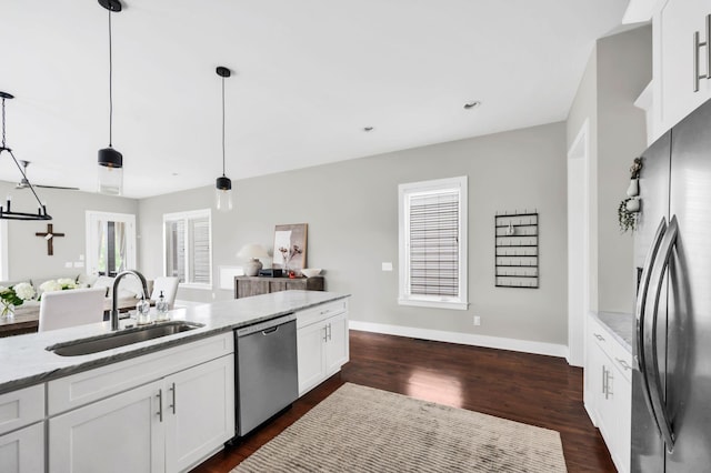 kitchen with sink, appliances with stainless steel finishes, pendant lighting, light stone countertops, and white cabinets