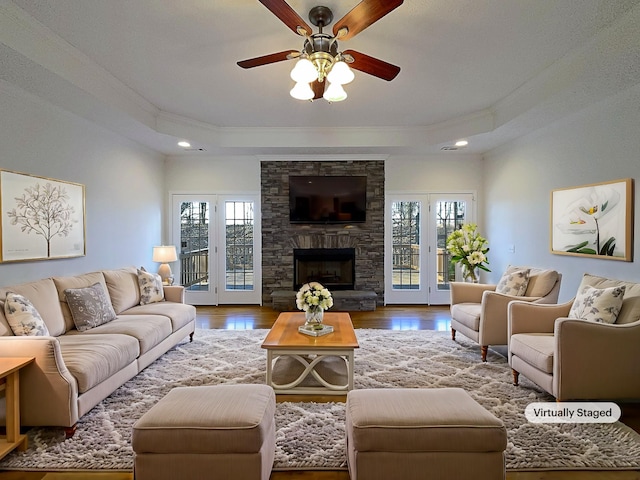 living room with hardwood / wood-style floors, a stone fireplace, a wealth of natural light, and a raised ceiling