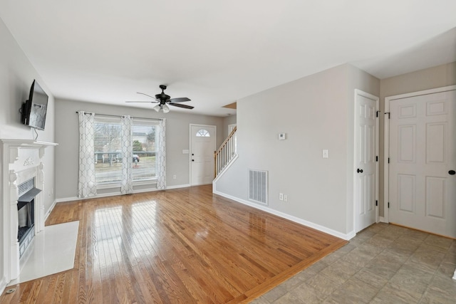 unfurnished living room with a premium fireplace, ceiling fan, and light wood-type flooring