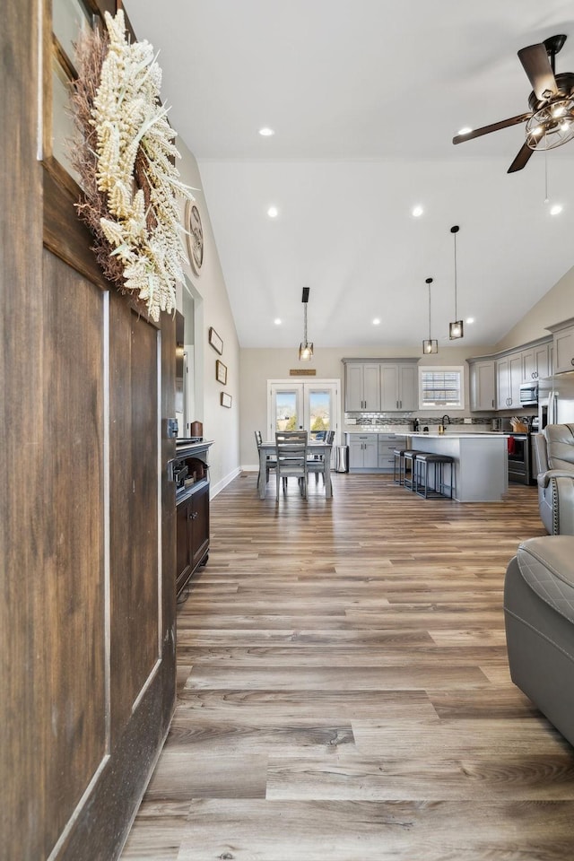 living room with ceiling fan, vaulted ceiling, and light wood-type flooring