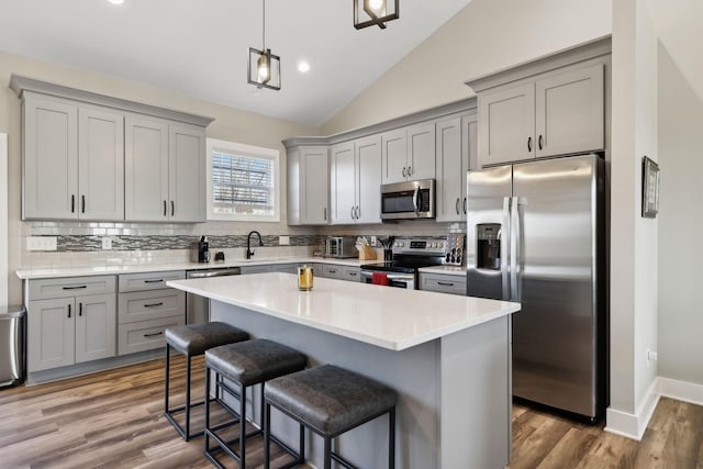 kitchen with a breakfast bar area, appliances with stainless steel finishes, a center island, decorative light fixtures, and vaulted ceiling