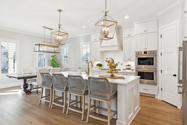 kitchen featuring pendant lighting, white cabinetry, an island with sink, and appliances with stainless steel finishes