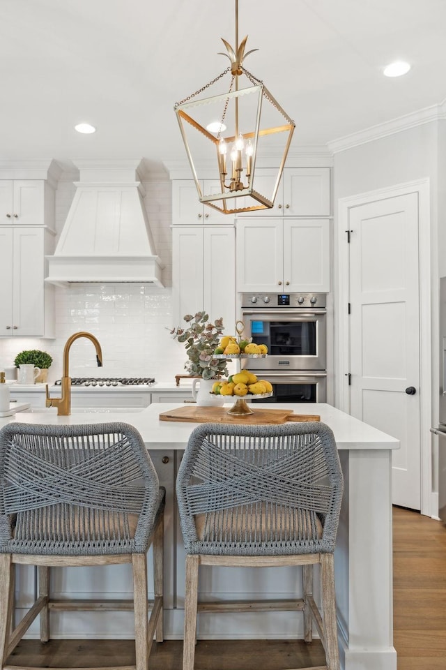 kitchen featuring white cabinetry, premium range hood, pendant lighting, and double oven