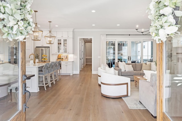 living room with an inviting chandelier, sink, crown molding, and light hardwood / wood-style floors