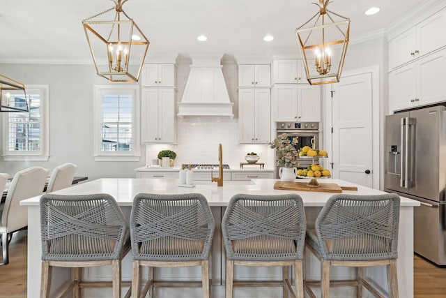 kitchen featuring custom exhaust hood, a center island with sink, appliances with stainless steel finishes, pendant lighting, and white cabinets