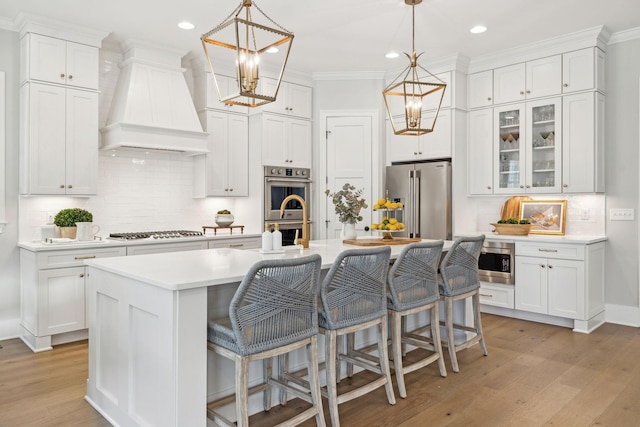 kitchen featuring white cabinetry, a center island with sink, stainless steel appliances, and premium range hood