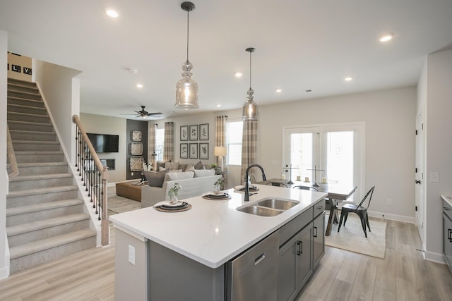 kitchen with decorative light fixtures, dishwasher, sink, a kitchen island with sink, and light hardwood / wood-style floors