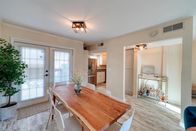 dining space featuring french doors, crown molding, and light wood-type flooring