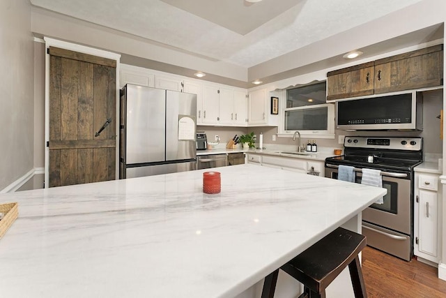 kitchen with appliances with stainless steel finishes, white cabinetry, sink, dark hardwood / wood-style flooring, and light stone counters