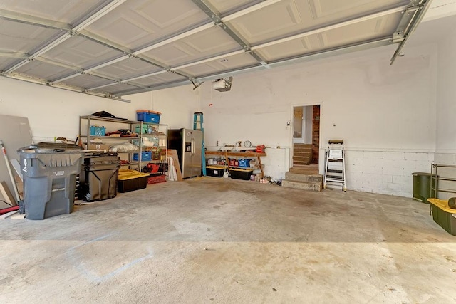 garage featuring a garage door opener and stainless steel refrigerator with ice dispenser