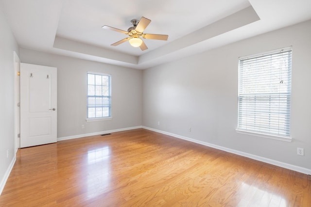 spare room with ceiling fan, a tray ceiling, and light hardwood / wood-style flooring