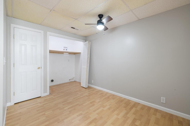 unfurnished bedroom with ceiling fan, a drop ceiling, light wood-type flooring, and a closet