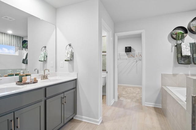 bathroom featuring vanity, wood-type flooring, a relaxing tiled tub, and toilet