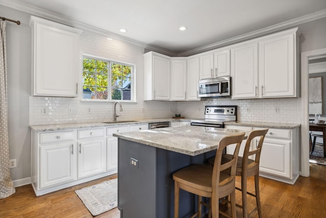 kitchen featuring stainless steel appliances, light stone countertops, a kitchen island, and white cabinets