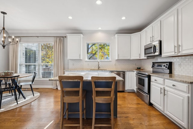 kitchen with stainless steel appliances, white cabinetry, light stone countertops, and a center island