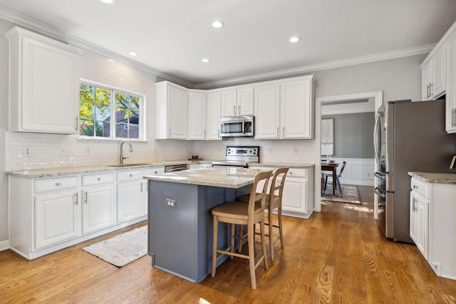 kitchen with sink, crown molding, white cabinetry, stainless steel appliances, and a kitchen island